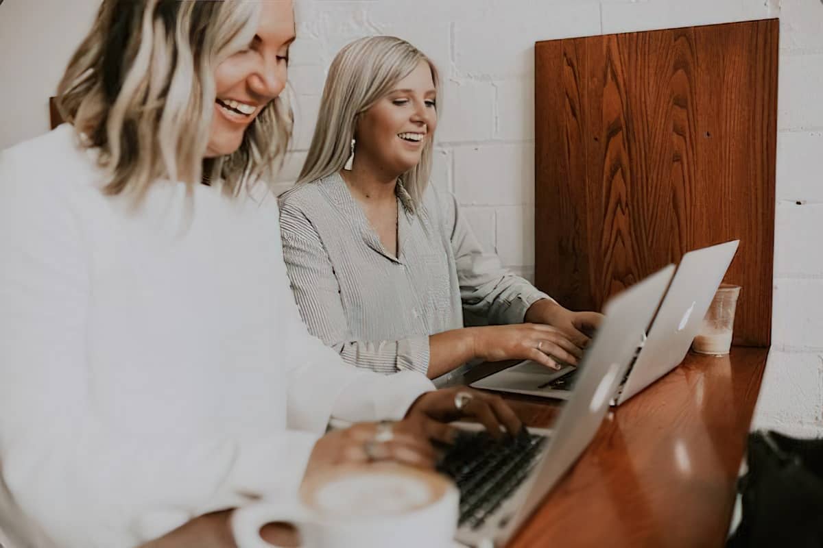 two women using laptops and laughing