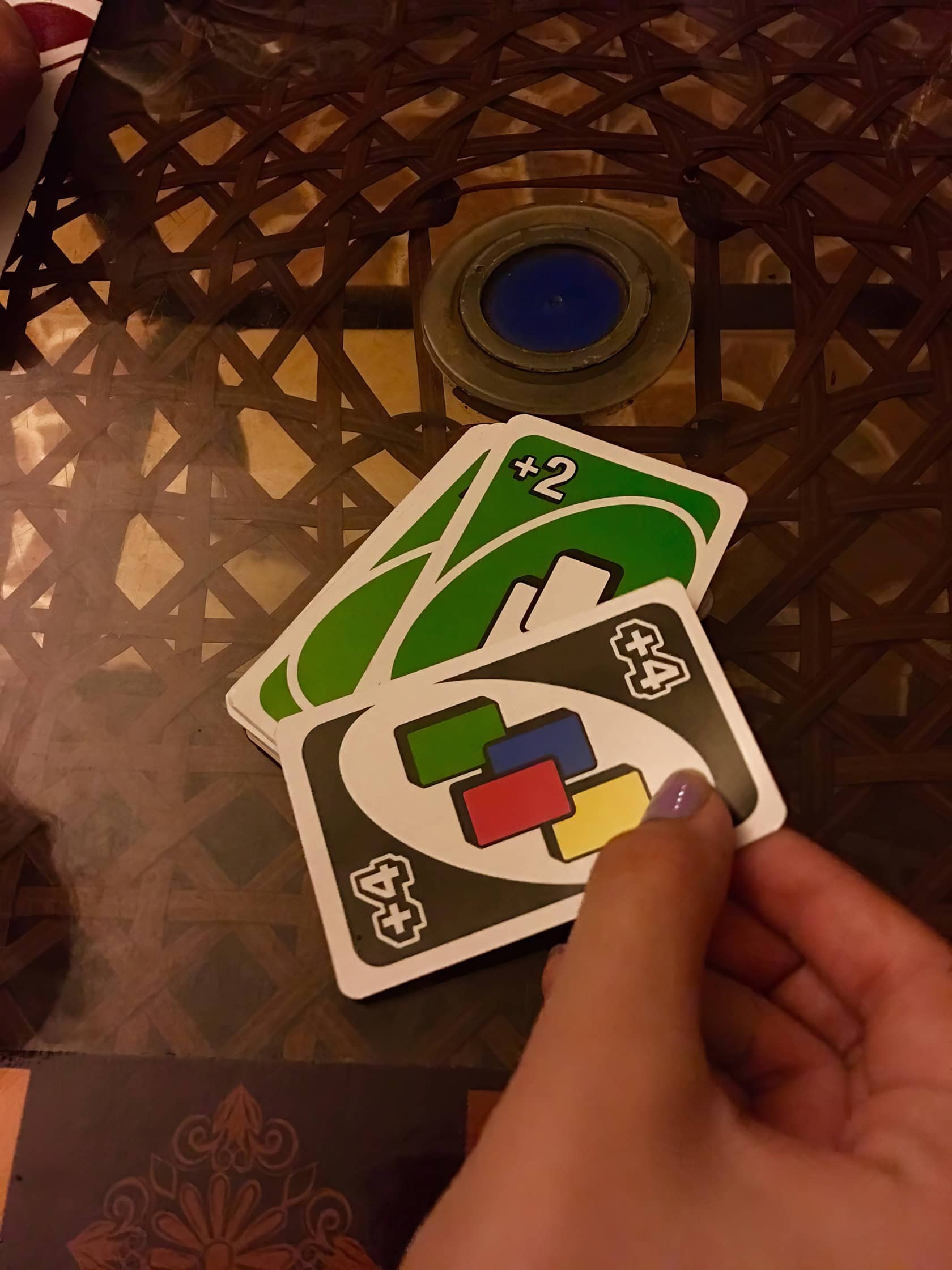 A game of Uno in progress on a well-worn wooden table with scattered cards. Can You Stack In Uno 3