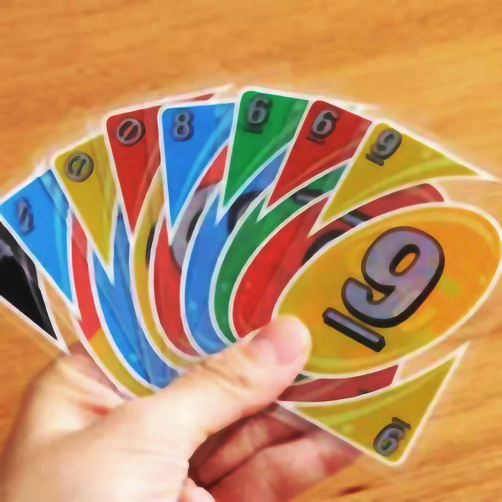 A teenage boy plays Uno Splash with friends on a weathered wooden picnic table in a sun-dappled garden. UNO Splash cards 1