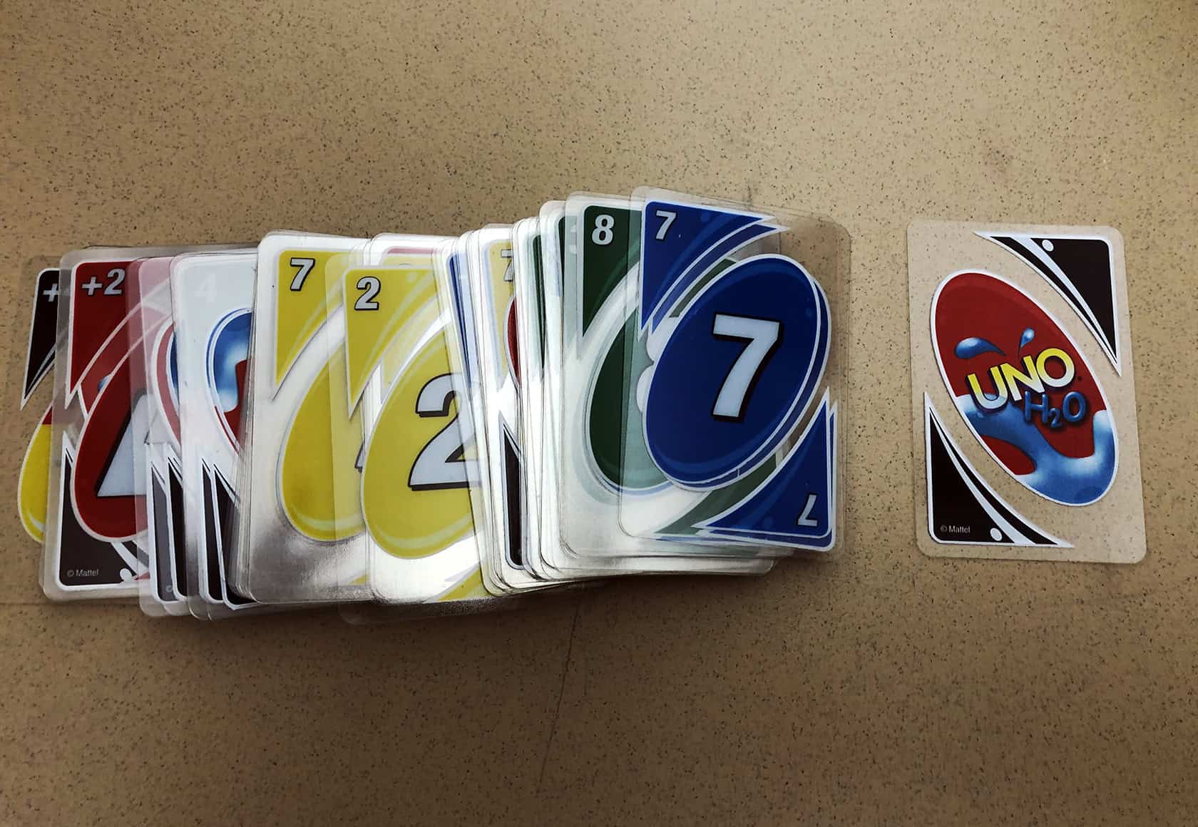 Five friends gather around a distressed wooden table, sharing genuine smiles and playing Uno in a warm, intimate setting. UNO Splash cards 2