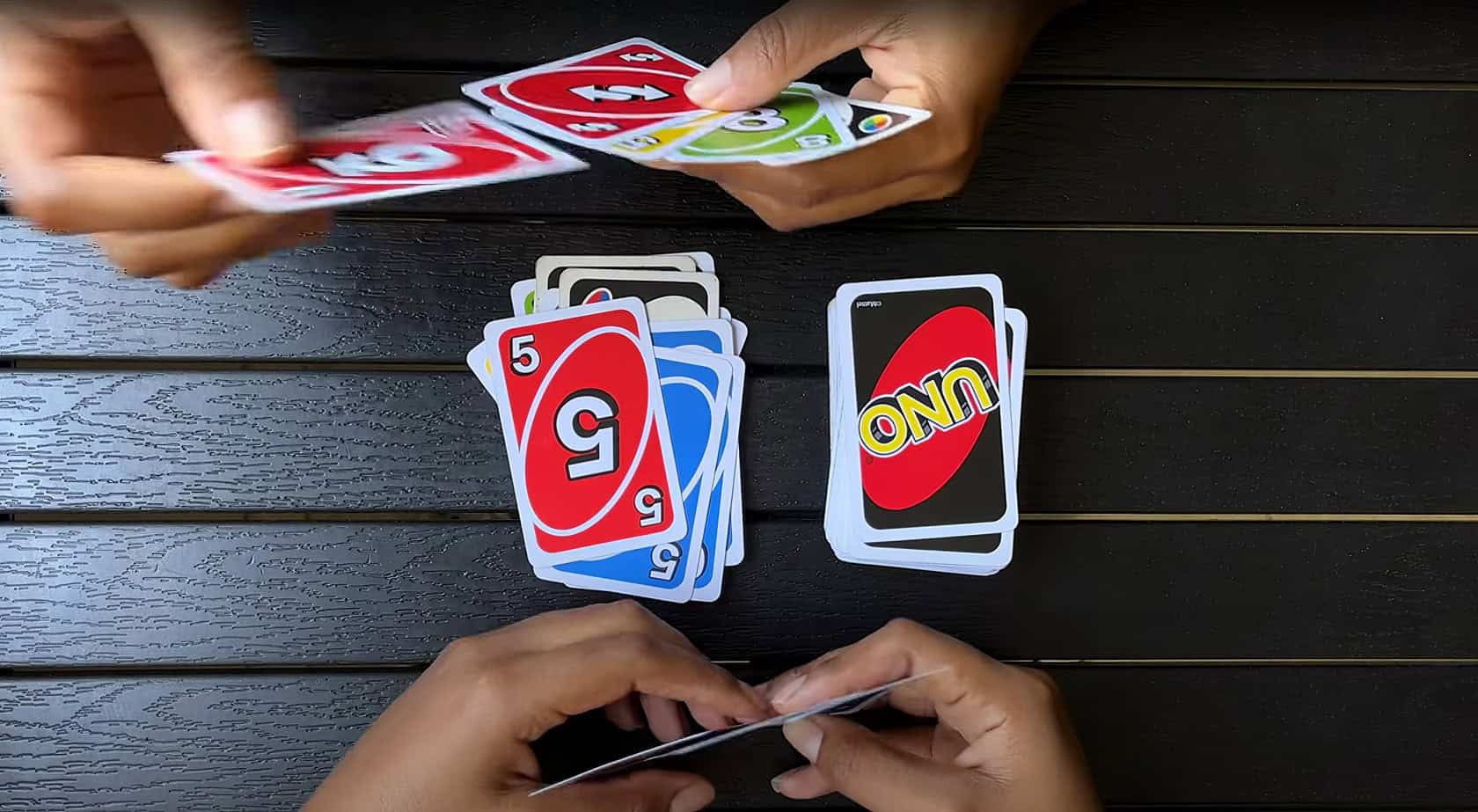 Five friends in their early 30s gather around a coffee table, playing cards and enjoying each other's company in a warmly lit living room. What Does The Shuffle Hands Card Mean In UNO 1