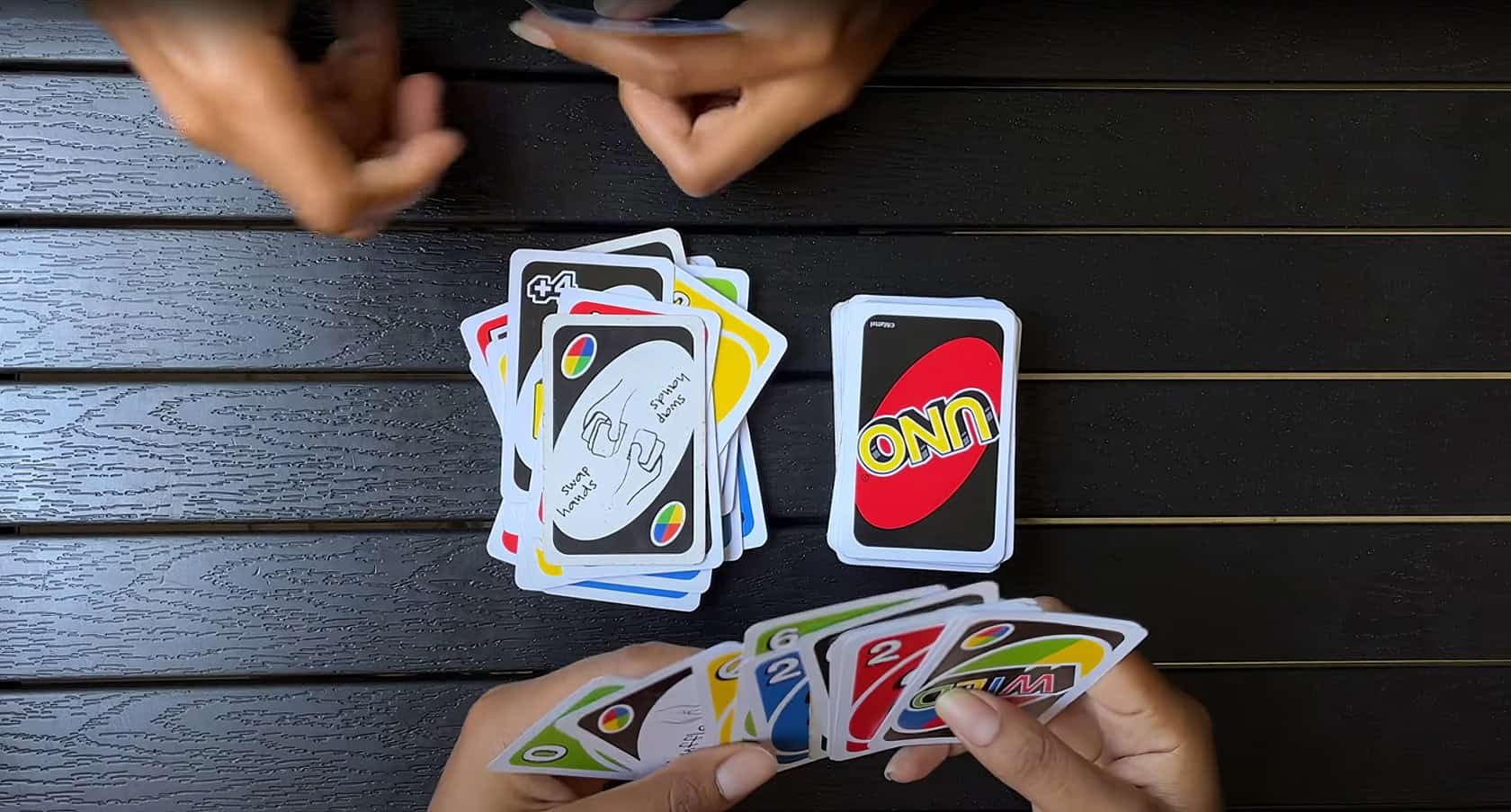 A group of friends playing cards at a wooden dining table in an intense and focused manner. What Does The Shuffle Hands Card Mean In UNO 3