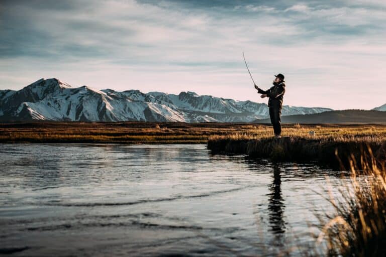 woman fly fishing with mountians in the background