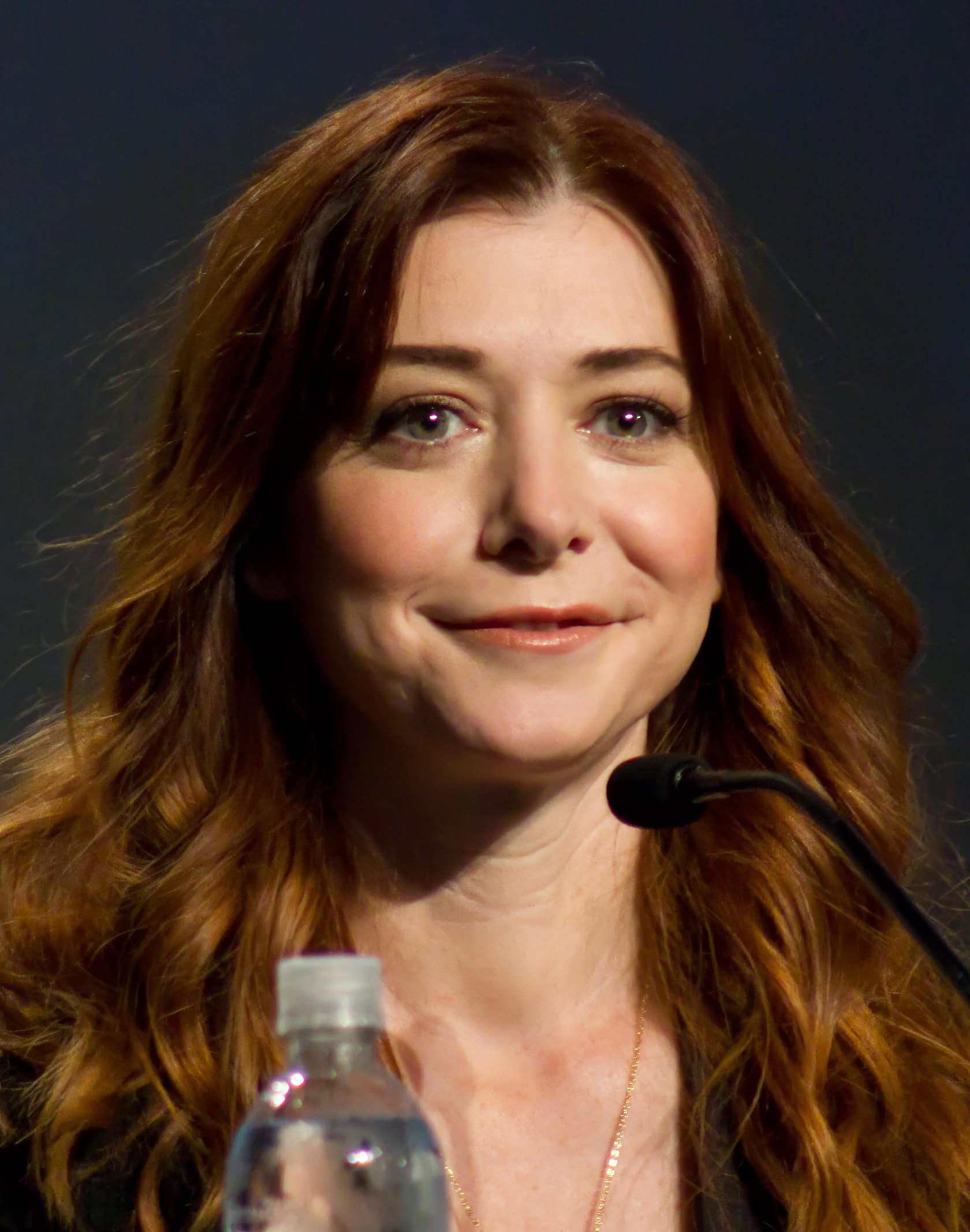 A woman in a cozy living room, surrounded by comic books and ambient light, smiles contentedly. Alyson Hannigan