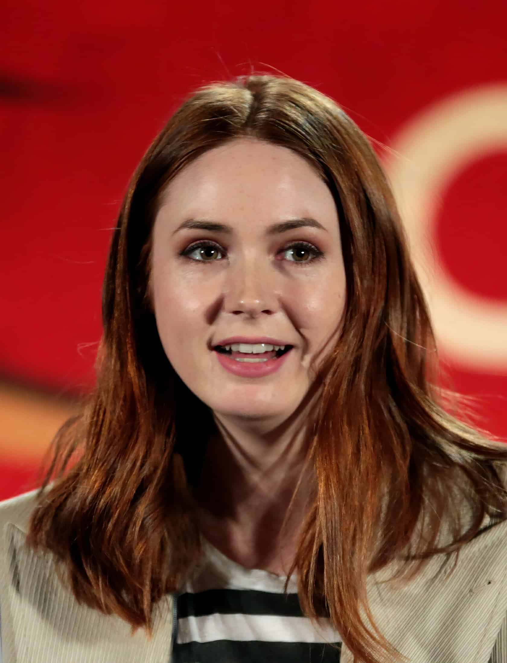 A woman in her 30s sits in a cluttered room surrounded by her comic book and action figure collection. Karen Gillan