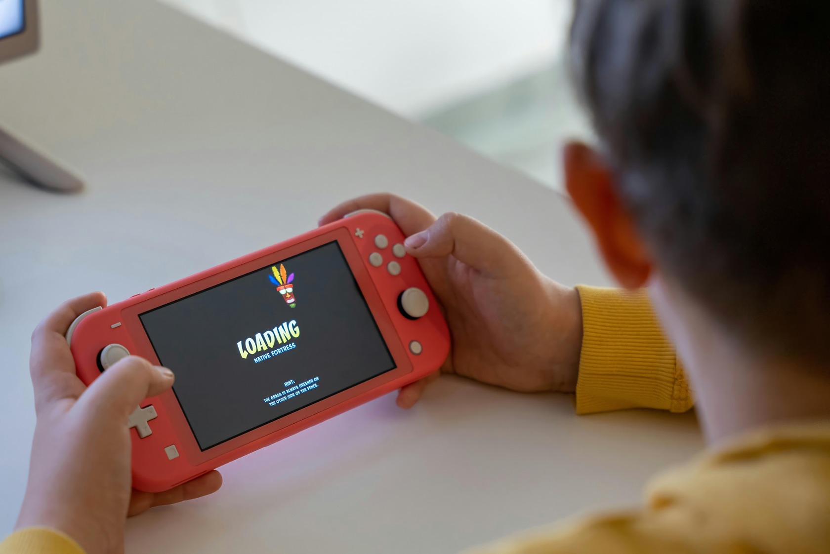 A lived-in wooden desk features a Nintendo Switch, game cases, and a computer monitor, with earbuds and a coffee mug nearby. Free Nintendo Switch Games 2