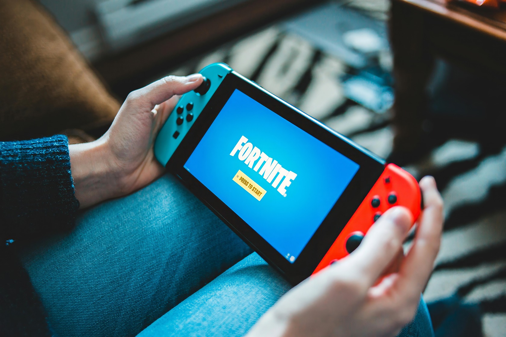 A young man in casual attire is intently playing a Nintendo Switch while seated on a cozy, worn sofa. Free Nintendo Switch Games 5