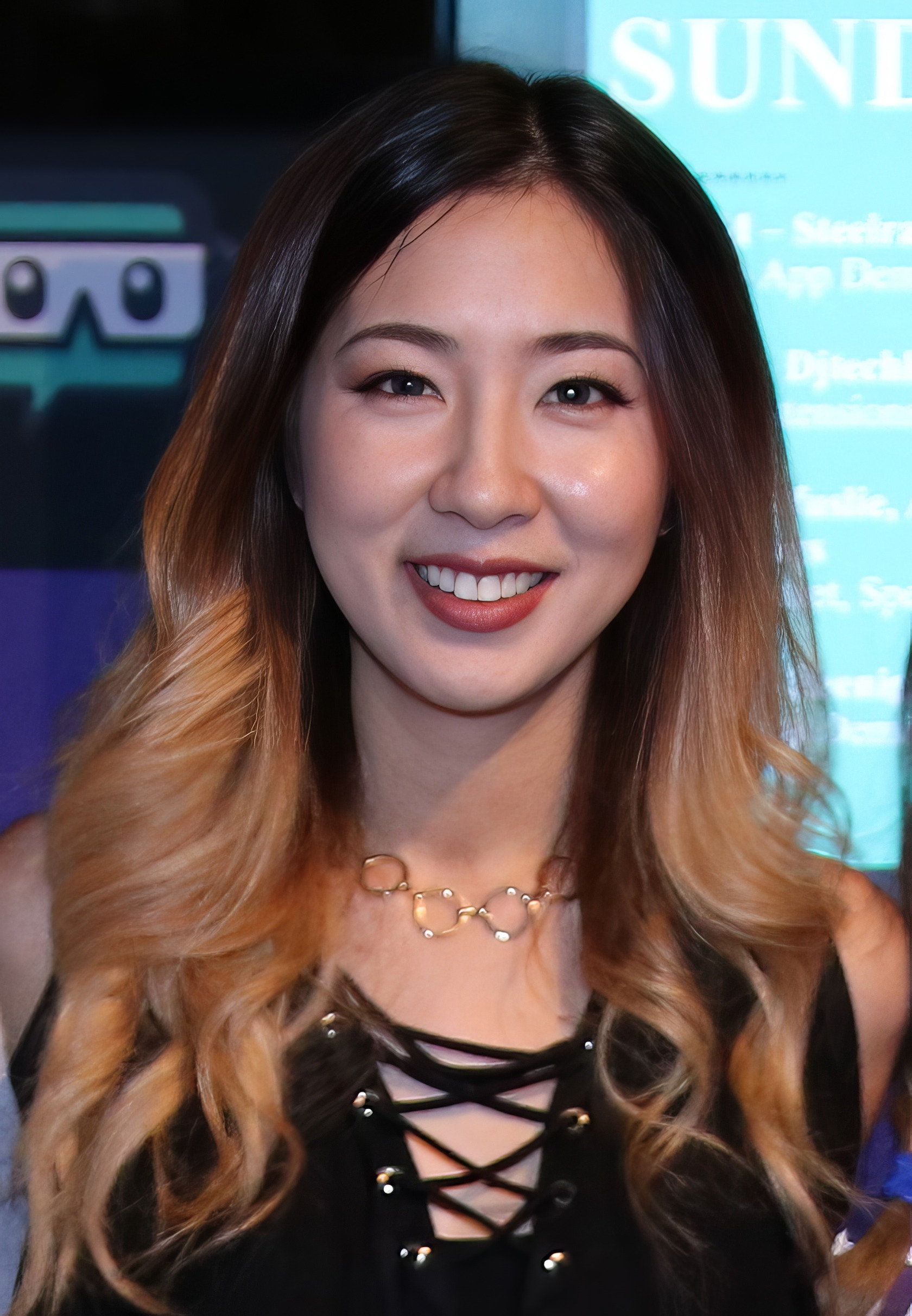 A woman in her 30s sits attentively at a gaming desk, focused on her mechanical keyboard and screen. Fuslie