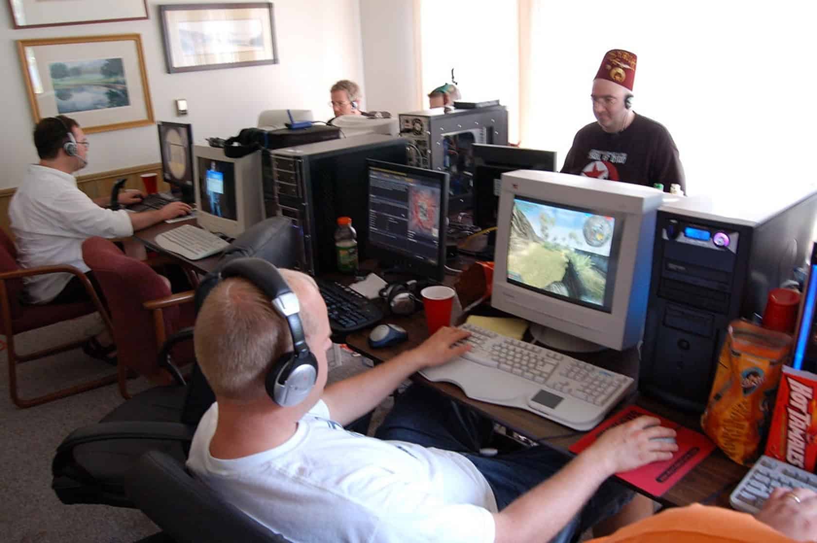 A wooden table is filled with snacks and beverages, surrounded by organized technical equipment and a person in concentration. What Do You Need for LAN Party Fun 3