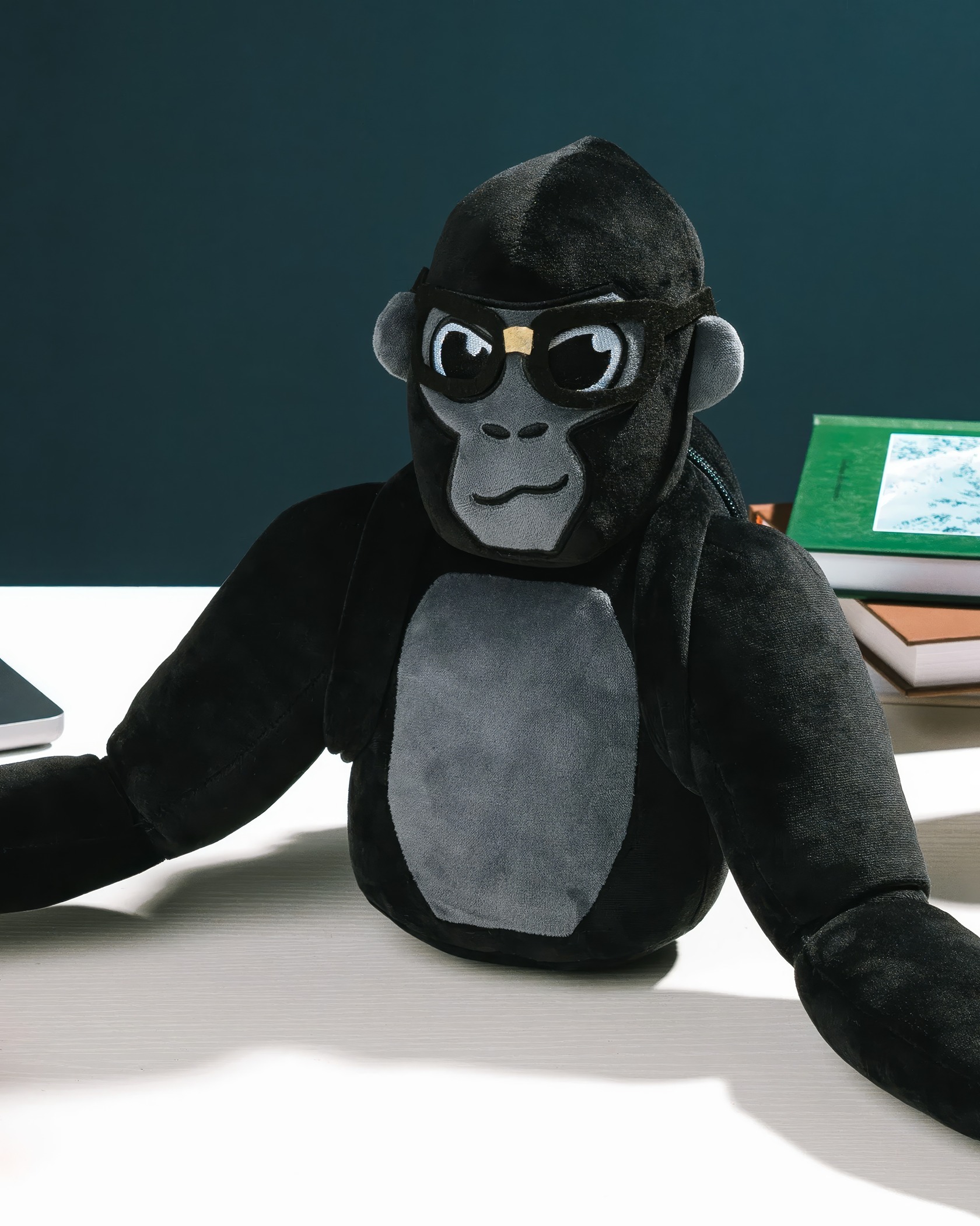 Gorilla Tag Plush: 7 Fan-Favorite Designs & Why Gamers Love Them 4 Soft plush monkey doll wearing black glasses and hoodie sitting on a desk with books and laptop in the background.