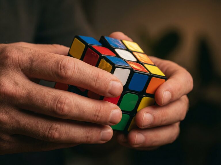 A person solving a colorful Rubik's Cube, showcasing focus and problem-solving skills. The image highlights classic brain teasers and intellectual challenges suitable for all ages.