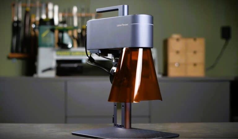 LaserPecker 3D laser engraving machine with a sleek design, set up on a workspace with tools in the background. Perfect for precision engraving on various materials with high accuracy.