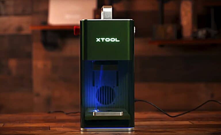 Smartphone-like device with a sleek design and LED lighting on a wooden surface, branded XTOOL, used for advanced technology or gaming purposes, placed in a modern indoor setting.