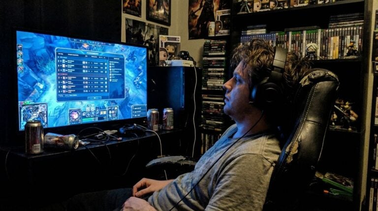 High-quality gaming setup for immersive online gameplay, featuring a large monitor, gaming chair, and headphones for optimal performance, surrounded by gaming collectibles and posters.