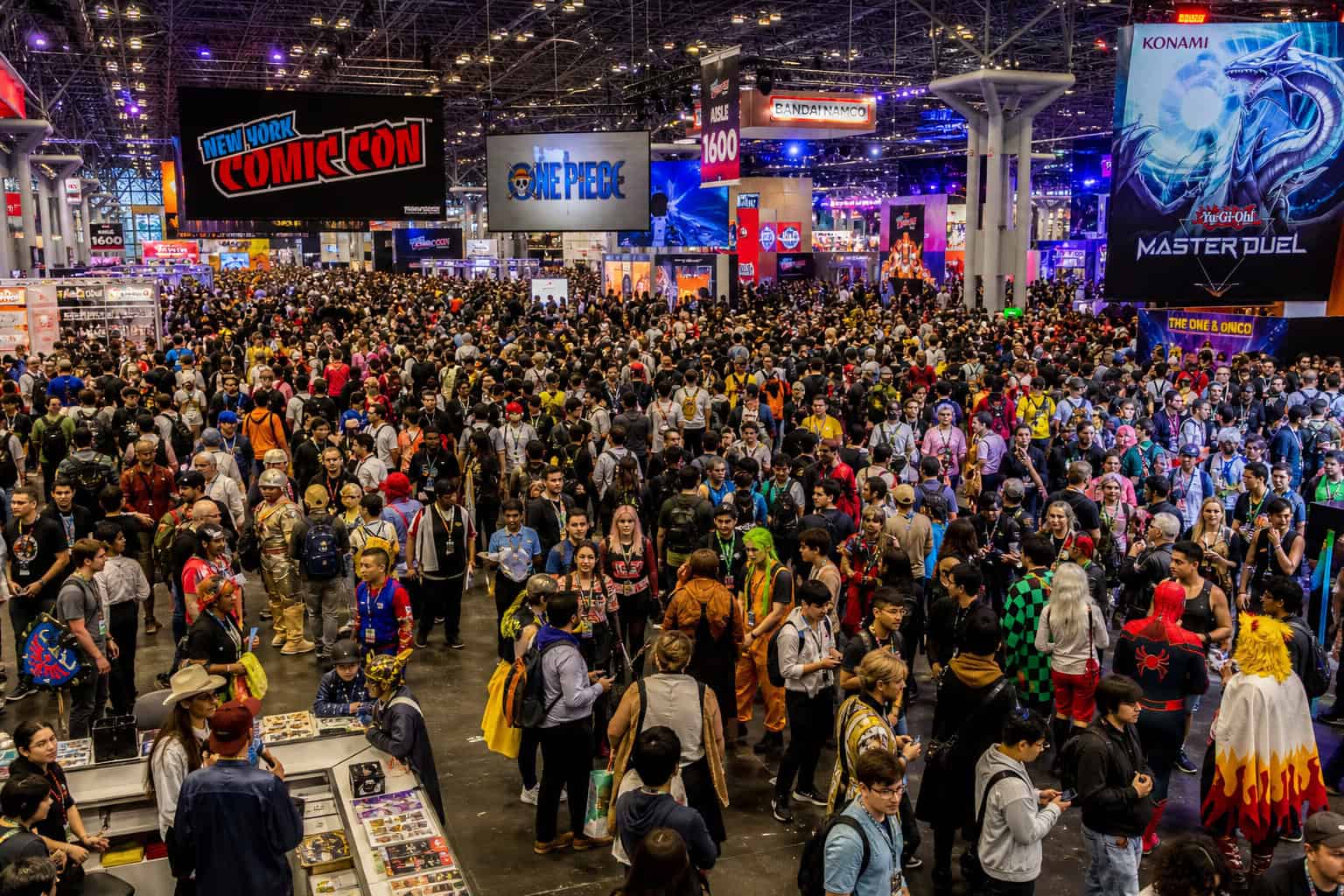 What Is Geek Culture? Psychology Confirms It’s Not Social Dysfunction 5 Vibrant crowd attending a large comic convention with various booths, banners, and displays including popular franchises like One Piece and Konami, showcasing a lively and energetic pop culture event.