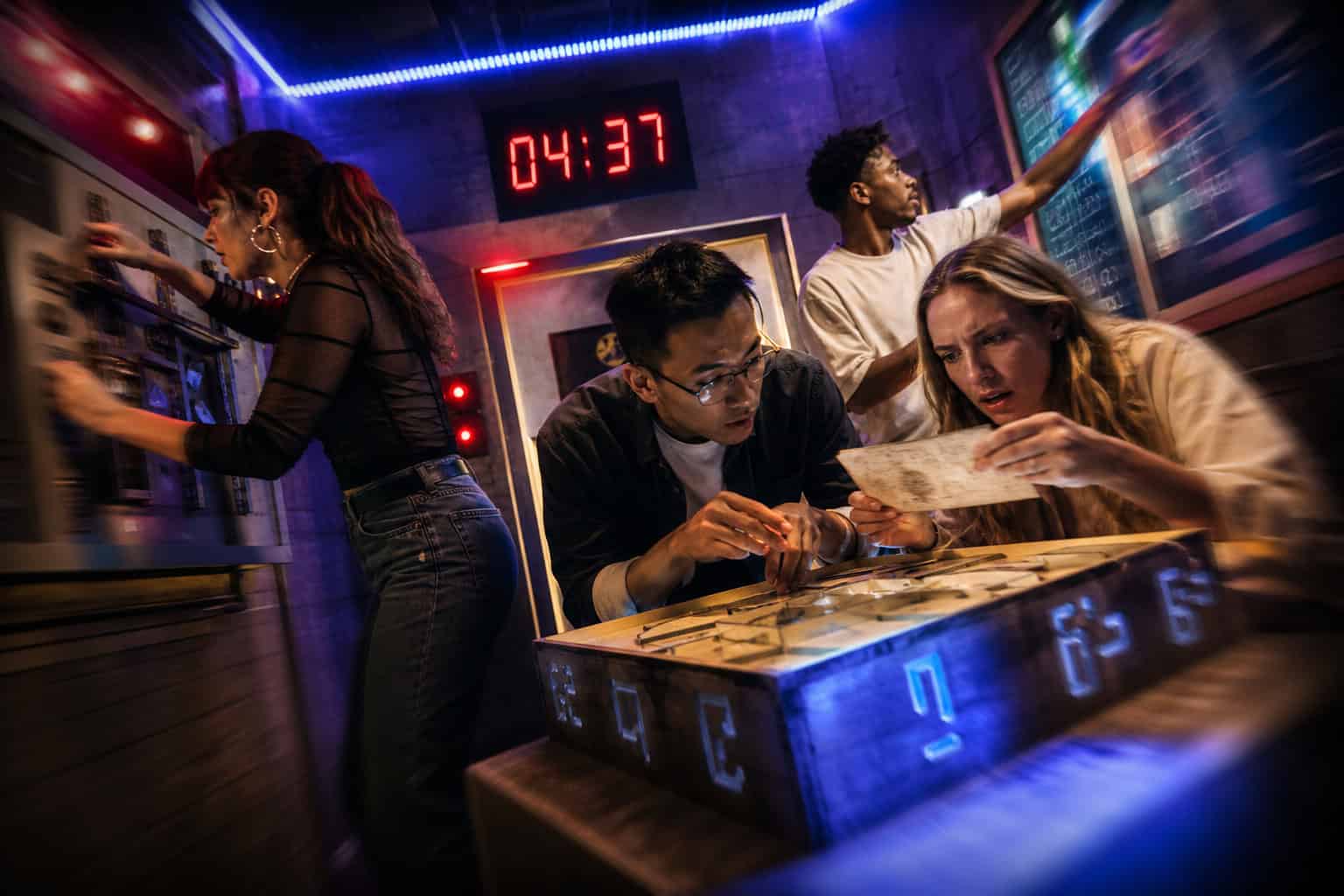 How To Make Friends As A Geek: Why Sandboxes Beat Social Mixers 6 Group of friends solving puzzles in an escape room at GeekExtreme, with a digital clock showing 04:37 in the background.