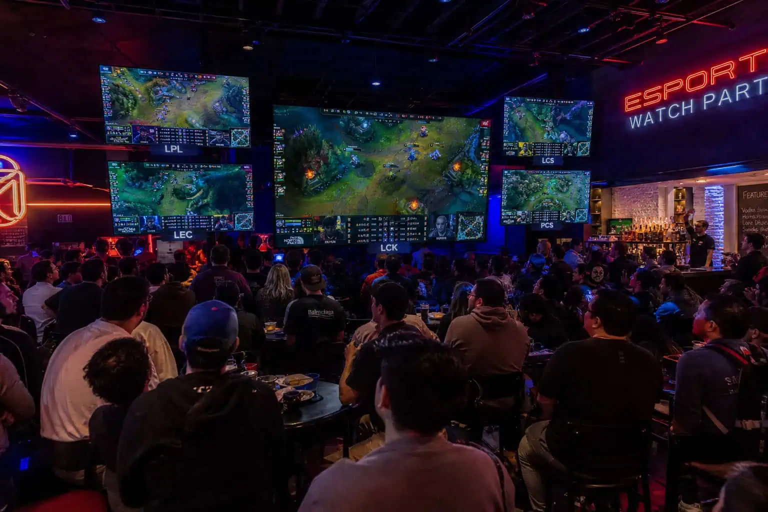 League of Legends Esports 2026: Full Tournament Calendar & Live Schedules 3 Crowd watching an esports tournament on large screens with gaming action and team logos, illuminated by vibrant LED lighting at GeekExtreme event.