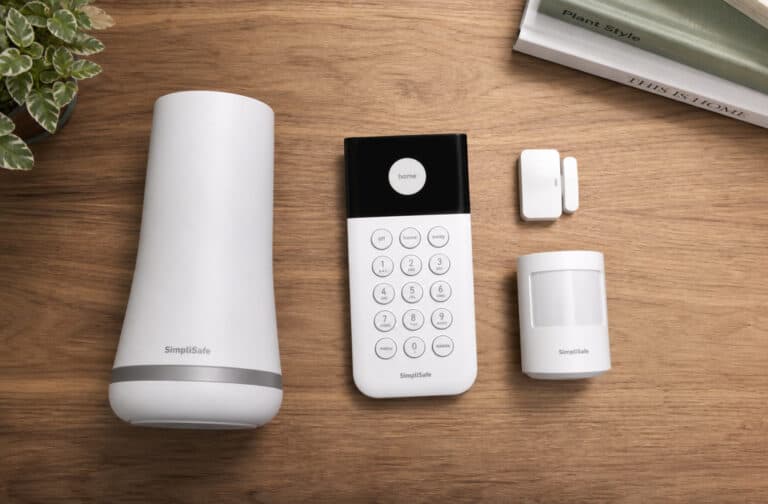 Smart home security devices including a motion sensor, remote control, and alarm system on a wooden surface.