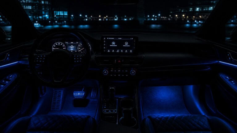 Interior of a luxury car illuminated with blue ambient lighting, showing the dashboard, steering wheel, and center console at night.