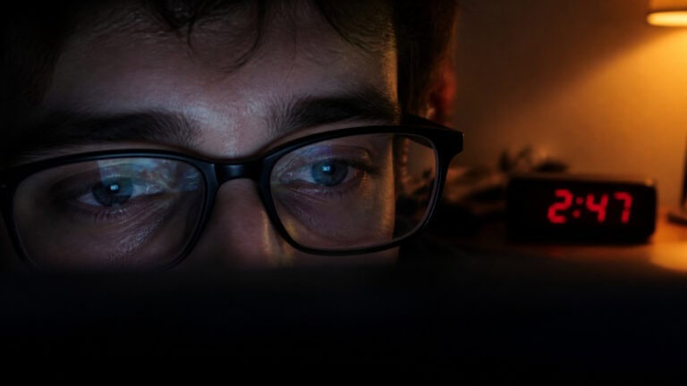 Close-up of a person with glasses working on a computer late at night, with a digital clock showing 2:47 in the background.