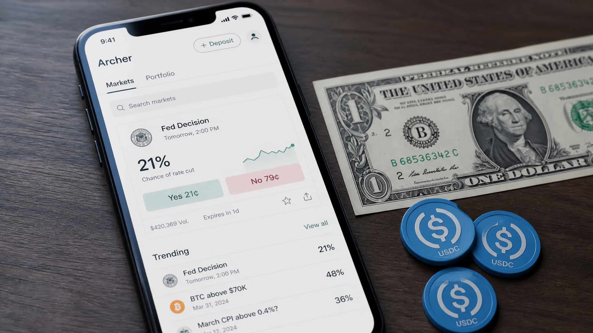 Smartphone displaying cryptocurrency trading app with Bitcoin and USDC options, next to a dollar bill and USDC coins on a wooden surface.