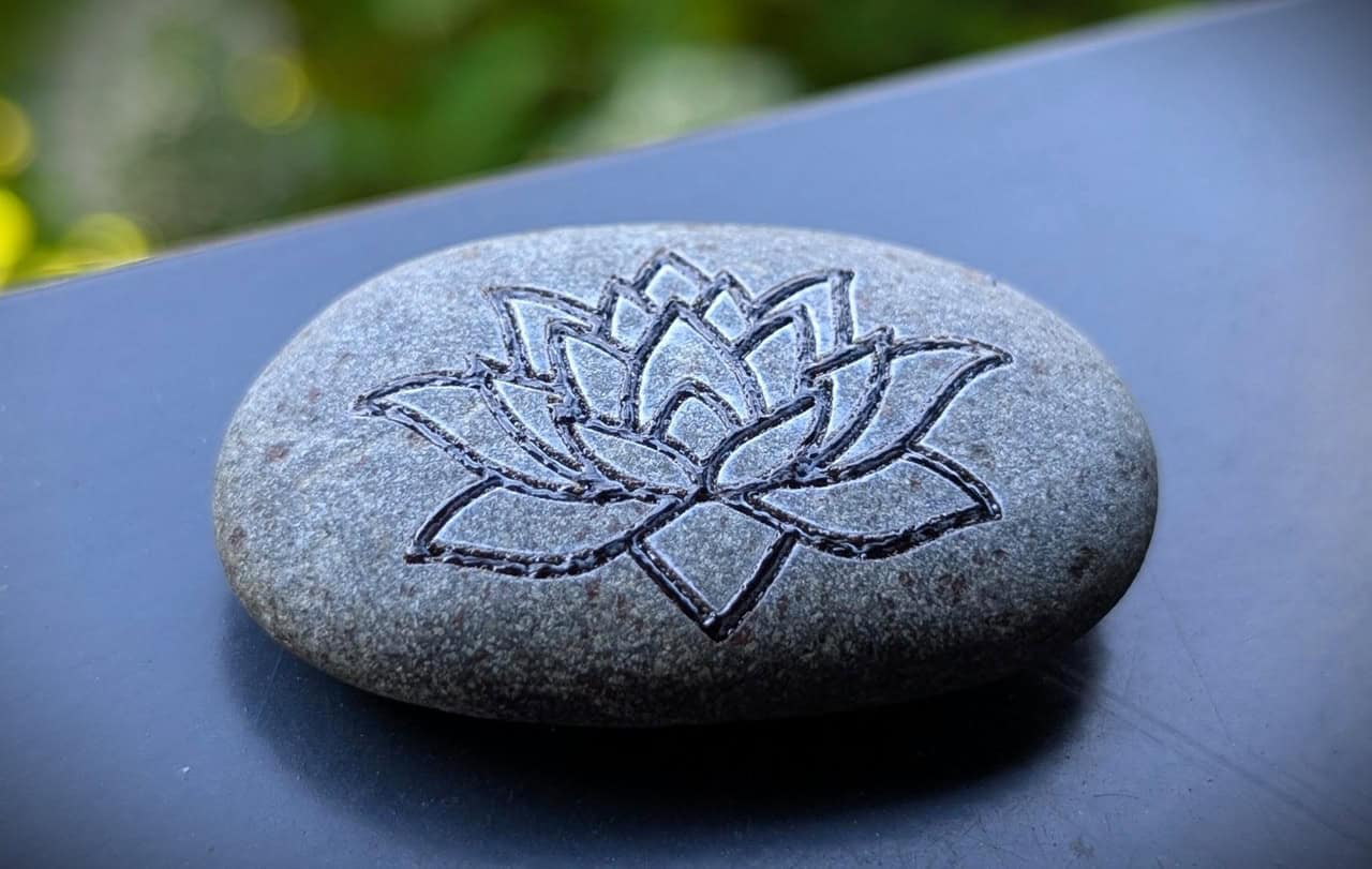WeCreat Lumos Flex Review: Where the Metal Claims End and MOPA Begins 8 Smooth gray stone engraved with a detailed lotus flower design, placed on a dark surface with blurred greenery in the background.