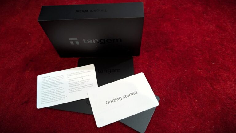 Image showing the Tangem Wallet box, user manual, and quick start guide on a red surface, highlighting the product's packaging and accessories.