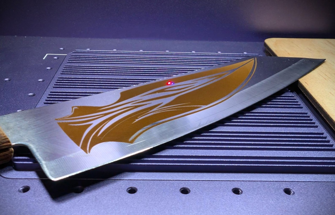 Is The WeCreat Lumos Flex The Best Metal Engraver? 6 Close-up of a metal engraving knife with a detailed design on the blade, placed on a work surface with a grid pattern, highlighting craftsmanship and precision.