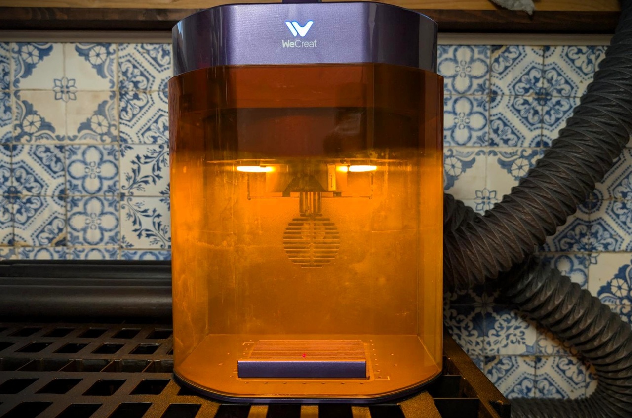 Close-up of the WeCreat Lumos Flex metal engraver with orange transparent casing and black flexible exhaust hose, used for precise metal engraving tasks.