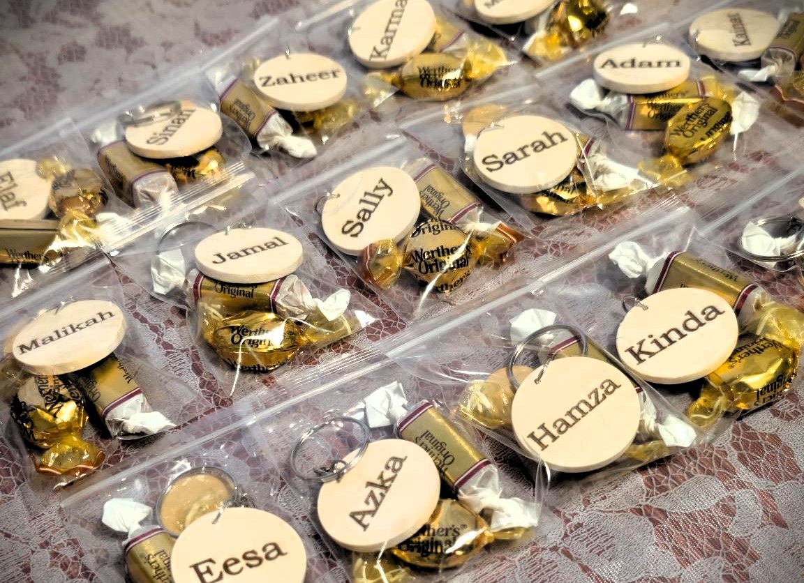 WeCreat Lumos Flex Review: Where the Metal Claims End and MOPA Begins 10 Custom keychains with individual names printed on round tags, attached to metal rings, arranged on a lace surface.