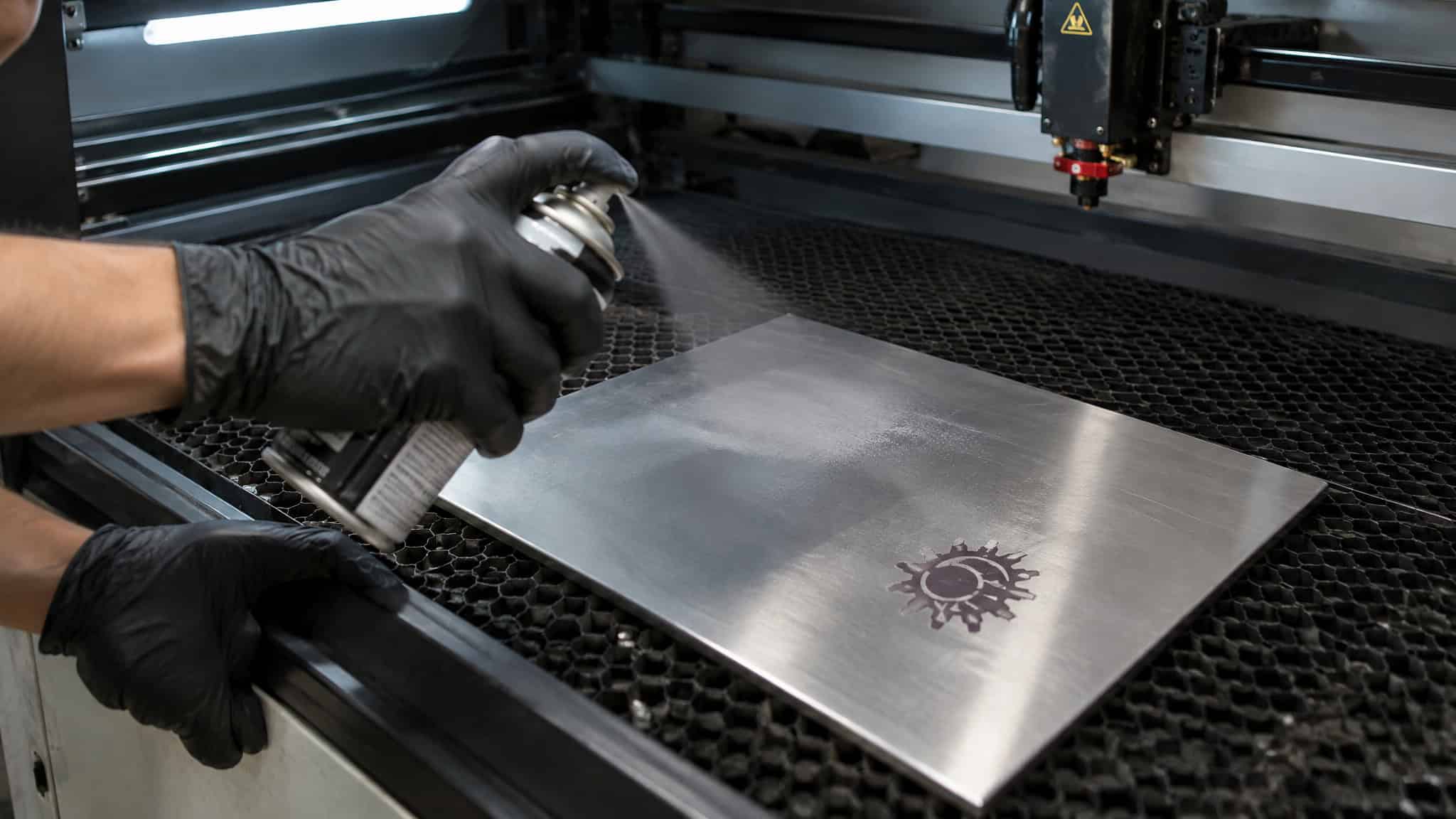 What Materials Can You Laser Engrave? A Wavelength-by-Material Compatibility Map 4 Close-up of a person wearing black gloves using a laser engraver to etch a design onto a metal sheet, with a visible laser beam and engraved pattern.
