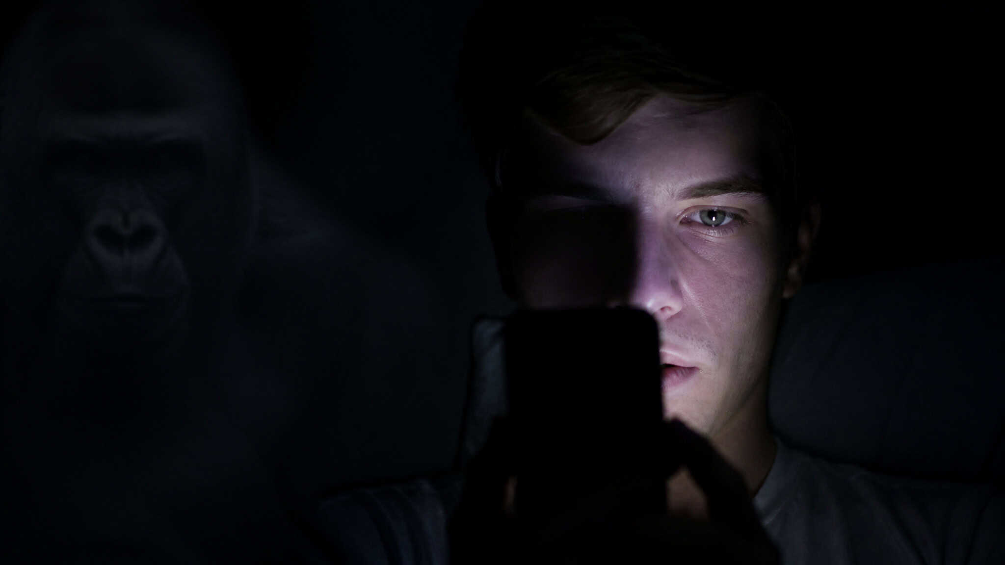 Person looking at phone with ghostly gorilla silhouette, illustrating inattentional blindness in ad perception.