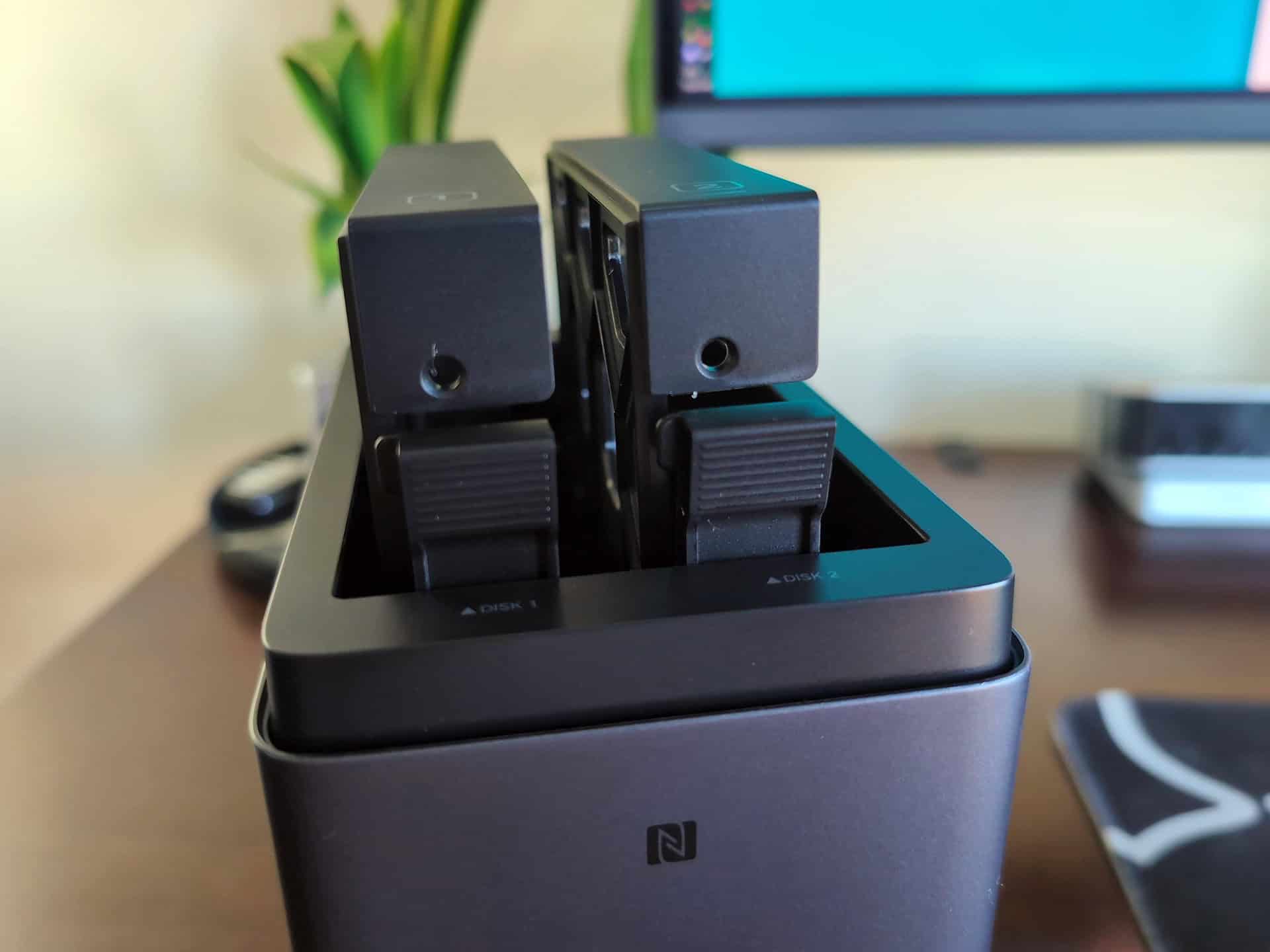 Ugreen DH2300 vs DXP2800 GT: Which Two-Bay NASync Should a First-Time Buyer Actually Get? 5 Two Ugreen NAS devices placed in a docking station on a desk, with a computer monitor and office supplies in the background.