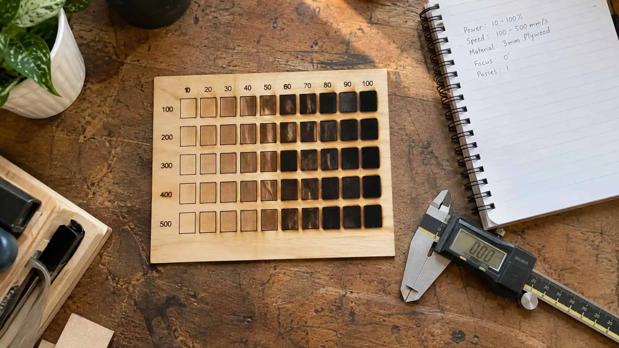 Laser Engraver Settings for Wood: Why the Same Numbers Fail on Different Boards 4 Test grid of laser burn squares on scrap plywood with a settings log notebook