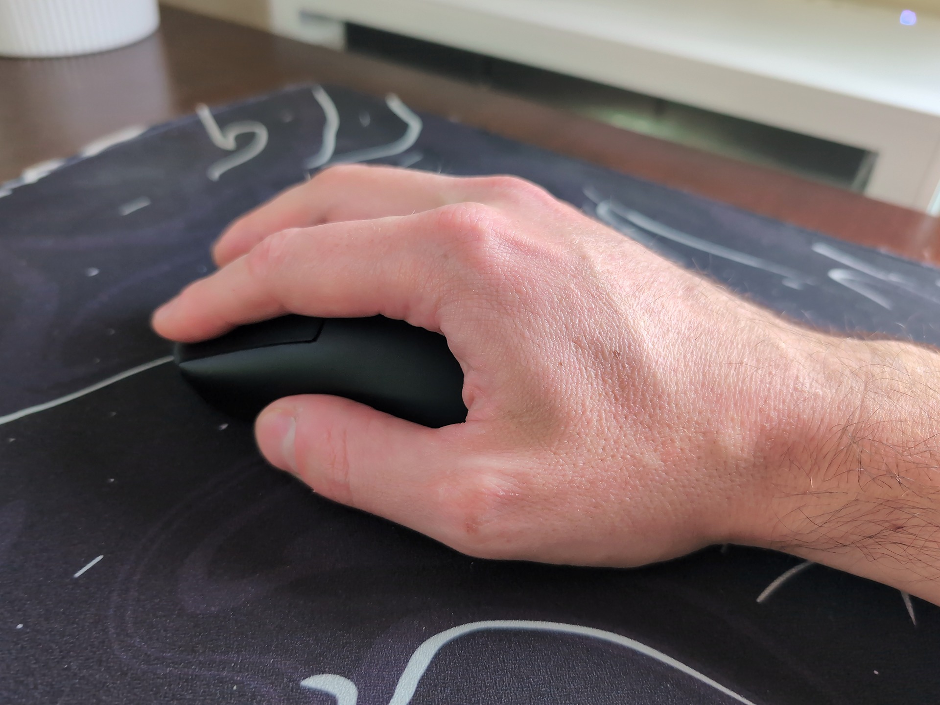 Rotary Mouse Review: 3 Weeks With the Dial That Replaced My Scroll Wheel 3 Close-up of a hand gripping a rotary mouse on a desk with a chalkboard surface, highlighting ergonomic design and user interaction.