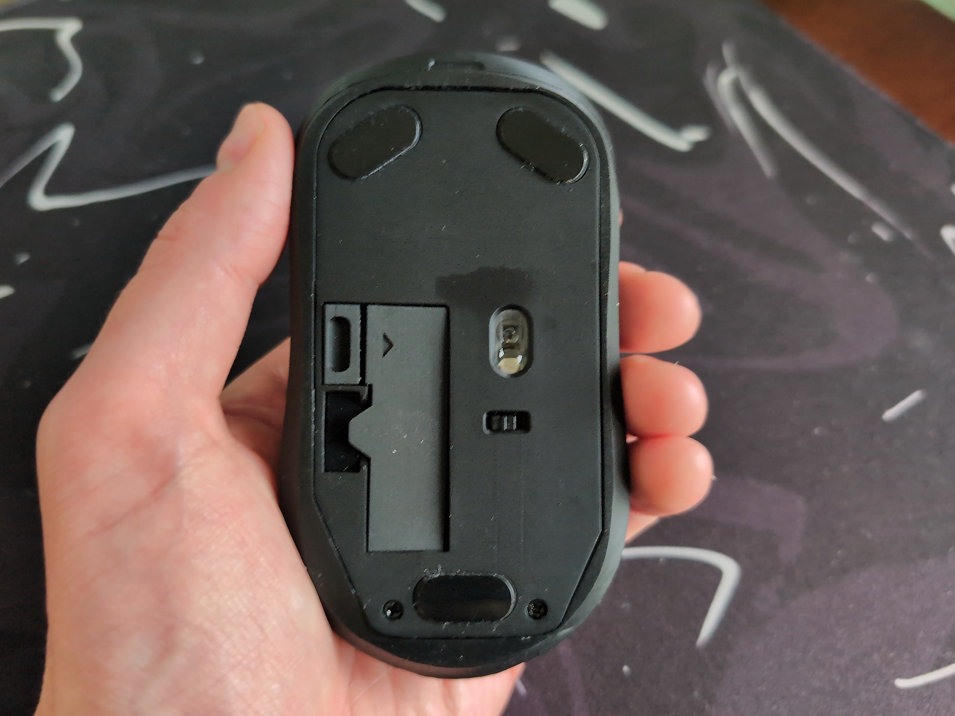 Rotary Mouse Review: 3 Weeks With the Dial That Replaced My Scroll Wheel 4 Close-up of a wireless rotary mouse held in a person's hand, showing the bottom side with a scroll dial and battery compartment.